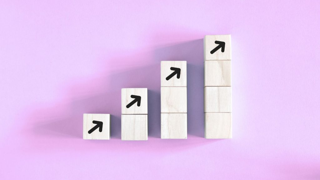 Stacked wooden blocks forming an upward staircase with arrows, symbolizing growth and progress.