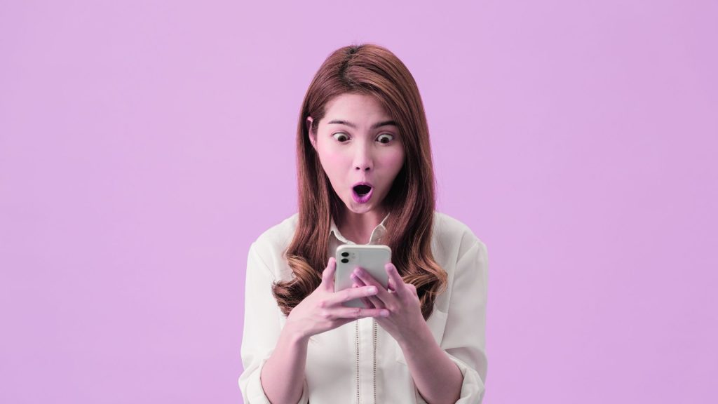 Woman looking surprised while holding and reading something on her smartphone.